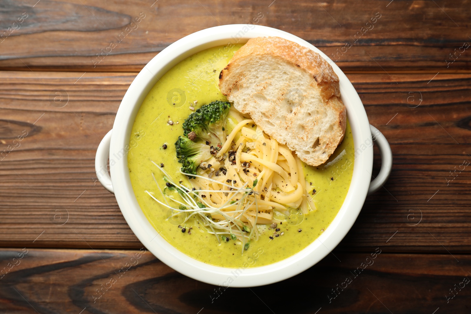 Photo of Delicious broccoli cream soup and crouton in bowl on wooden table, top view