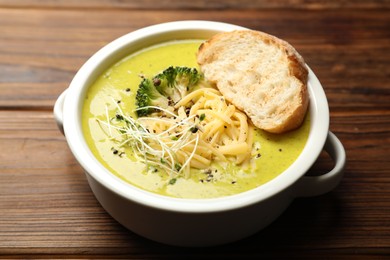 Photo of Delicious broccoli cream soup and crouton in bowl on wooden table, closeup