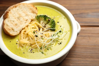 Photo of Delicious broccoli cream soup and crouton in bowl on wooden table, closeup