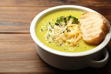 Photo of Delicious broccoli cream soup and crouton in bowl on wooden table, closeup. Space for text