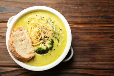 Photo of Delicious broccoli cream soup and crouton in bowl on wooden table, top view. Space for text