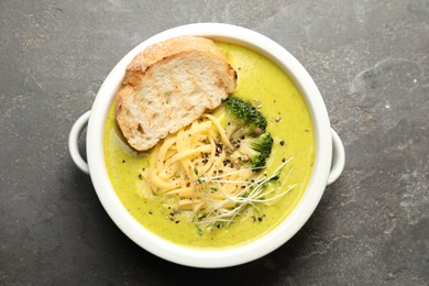 Photo of Delicious broccoli cream soup and crouton in bowl on gray textured table, top view