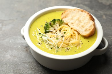 Photo of Delicious broccoli cream soup and crouton in bowl on gray textured table, closeup