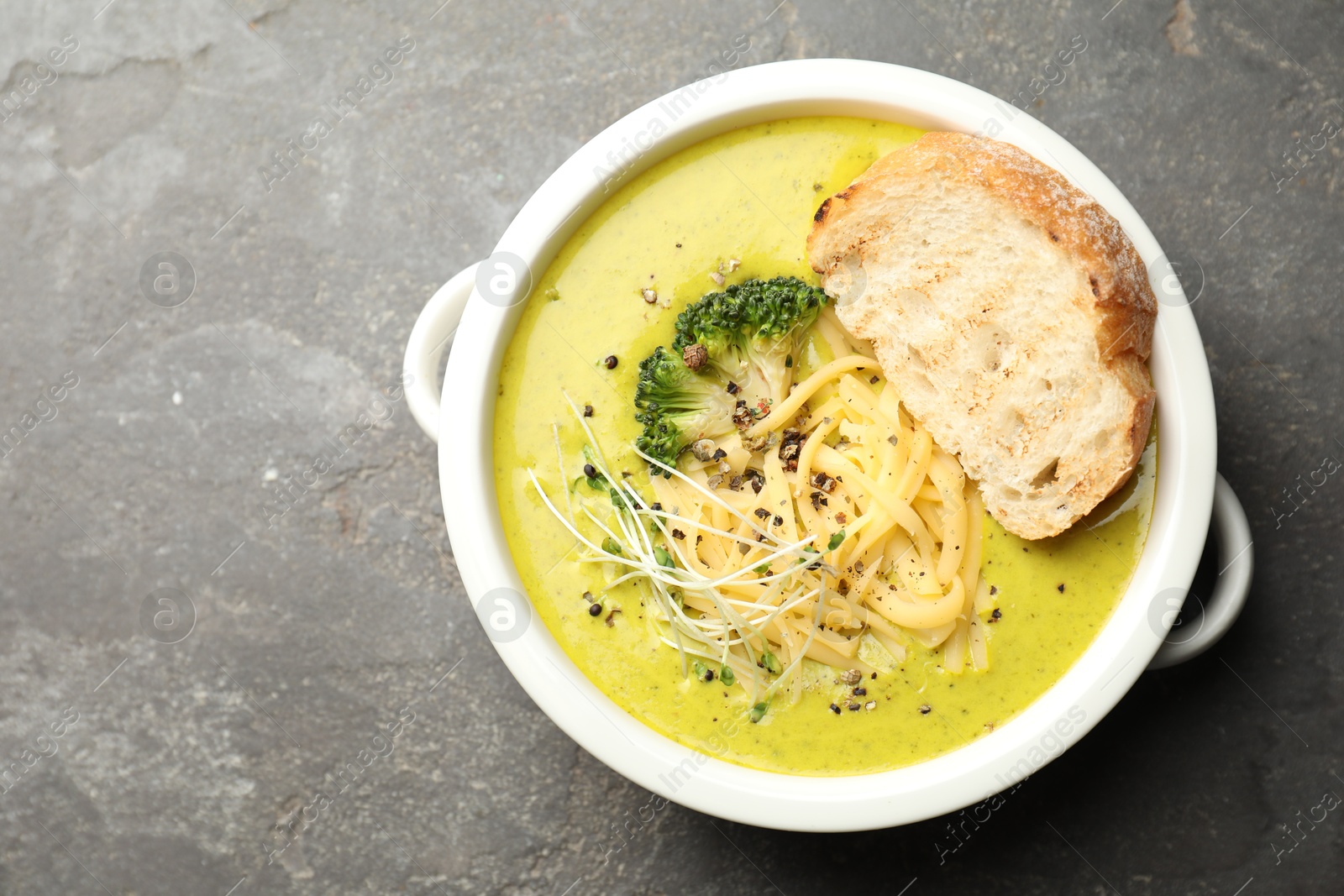 Photo of Delicious broccoli cream soup and crouton in bowl on gray textured table, top view. Space for text