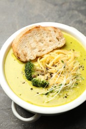 Photo of Delicious broccoli cream soup and crouton in bowl on gray textured table, above view