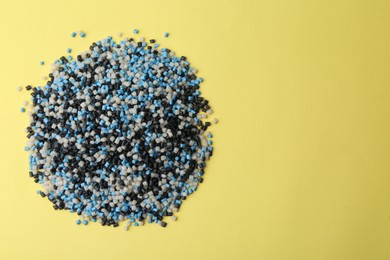 Pile of colorful plastic granules on yellow background, top view. Space for text