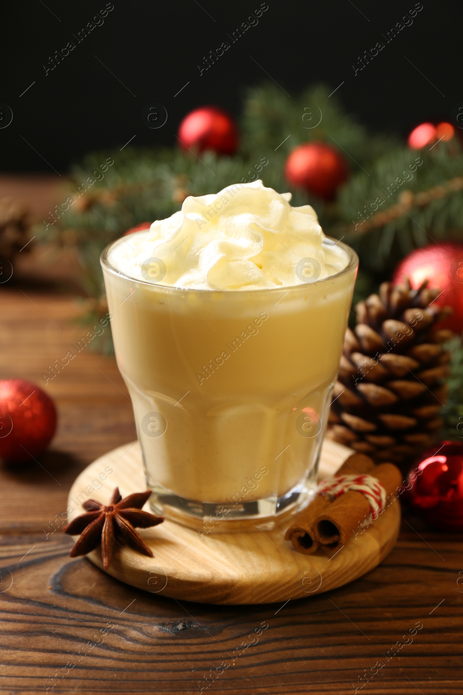 Photo of Tasty Christmas cocktail (eggnog) in glass and festive decor on wooden table, closeup