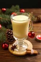 Photo of Tasty Christmas cocktail (eggnog) in glass, festive decor and burning candle on wooden table, closeup