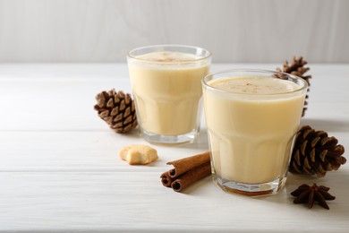 Photo of Tasty Christmas cocktail (eggnog) in glasses, pine cones and spices on white wooden table, closeup