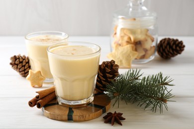 Photo of Tasty Christmas cocktail (eggnog) in glasses, pine cones and spices on white wooden table, closeup