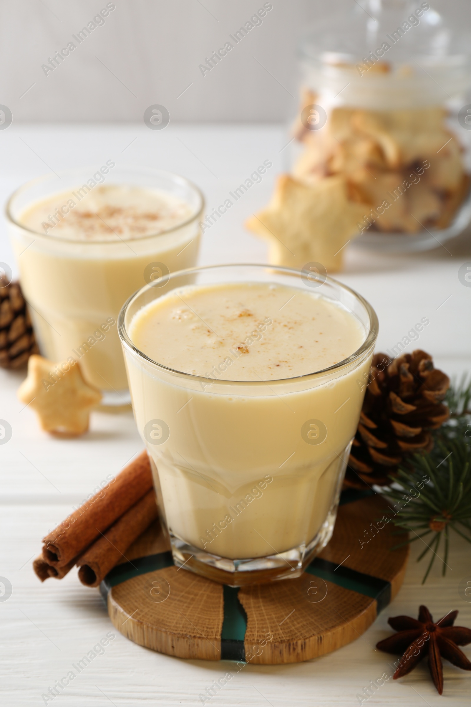 Photo of Tasty Christmas cocktail (eggnog) in glasses, pine cones and spices on white wooden table, closeup