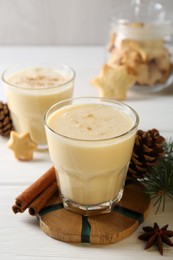 Photo of Tasty Christmas cocktail (eggnog) in glasses, pine cones and spices on white wooden table, closeup