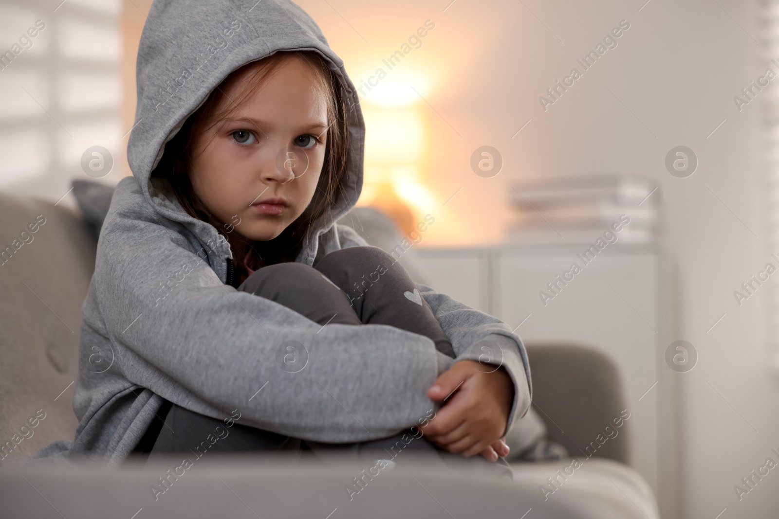 Photo of Orphanage concept. Sad girl sitting on sofa indoors