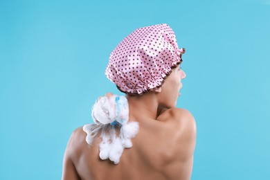 Man with shower cap and mesh sponge on light blue background