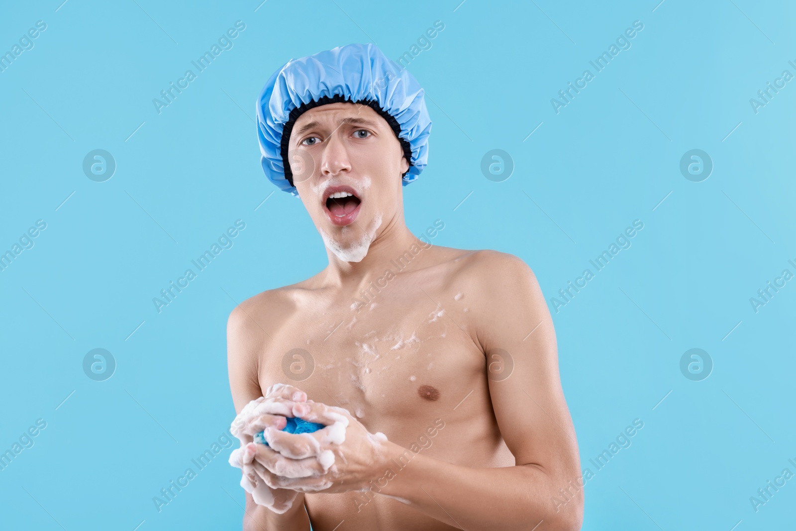 Photo of Man with shower cap and mesh sponge on light blue background