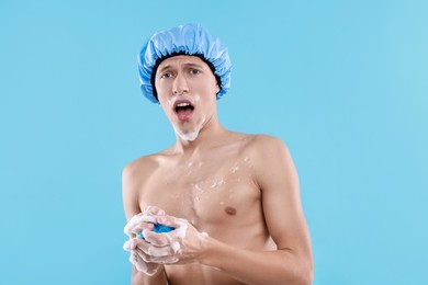 Photo of Man with shower cap and mesh sponge on light blue background