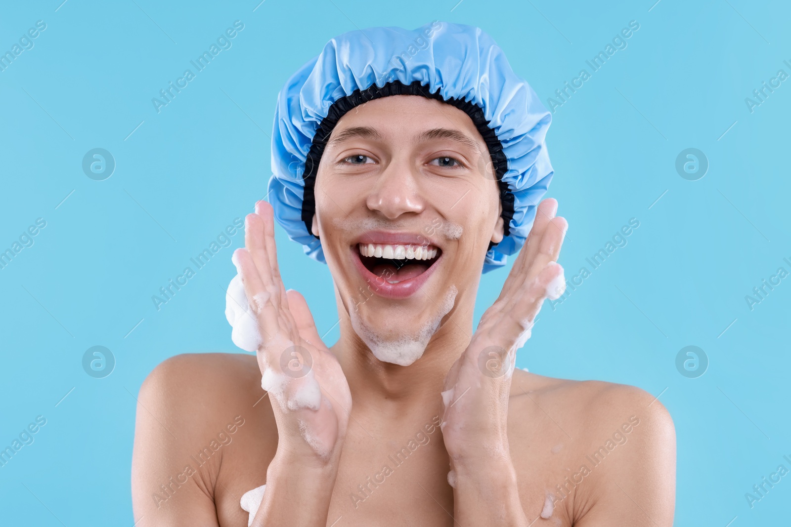 Photo of Man in shower cap covered with soap foam on light blue background