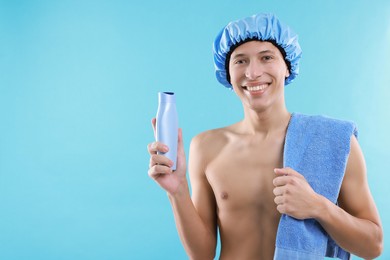 Man with shower cap, shampoo and towel on light blue background, space for text