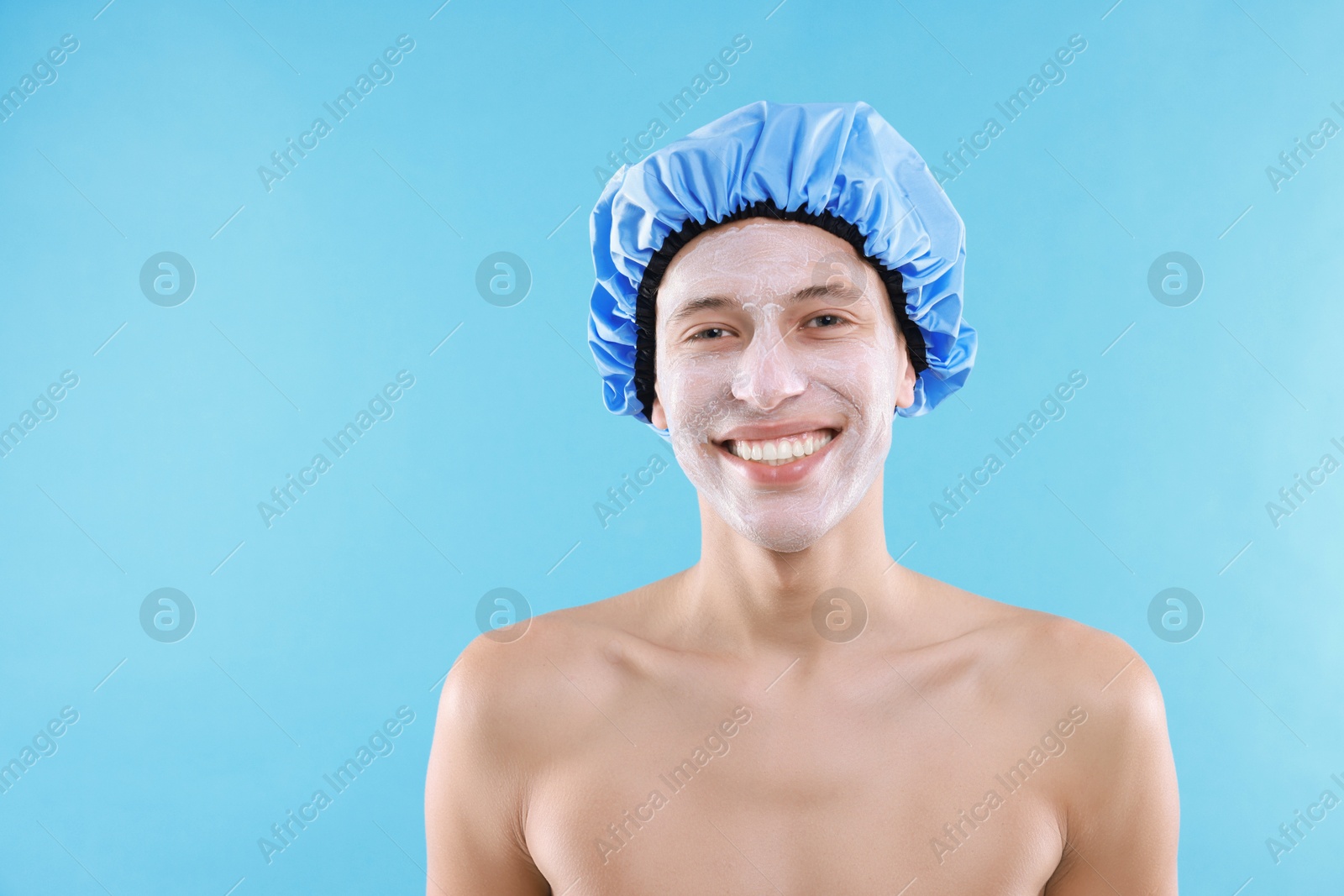 Photo of Man in shower cap with cream on his face against light blue background, space for text