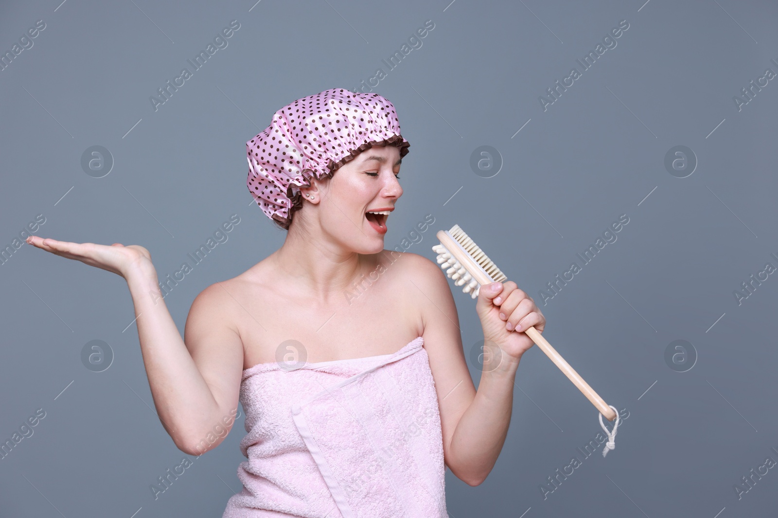 Photo of Woman with shower cap and brush singing on grey background