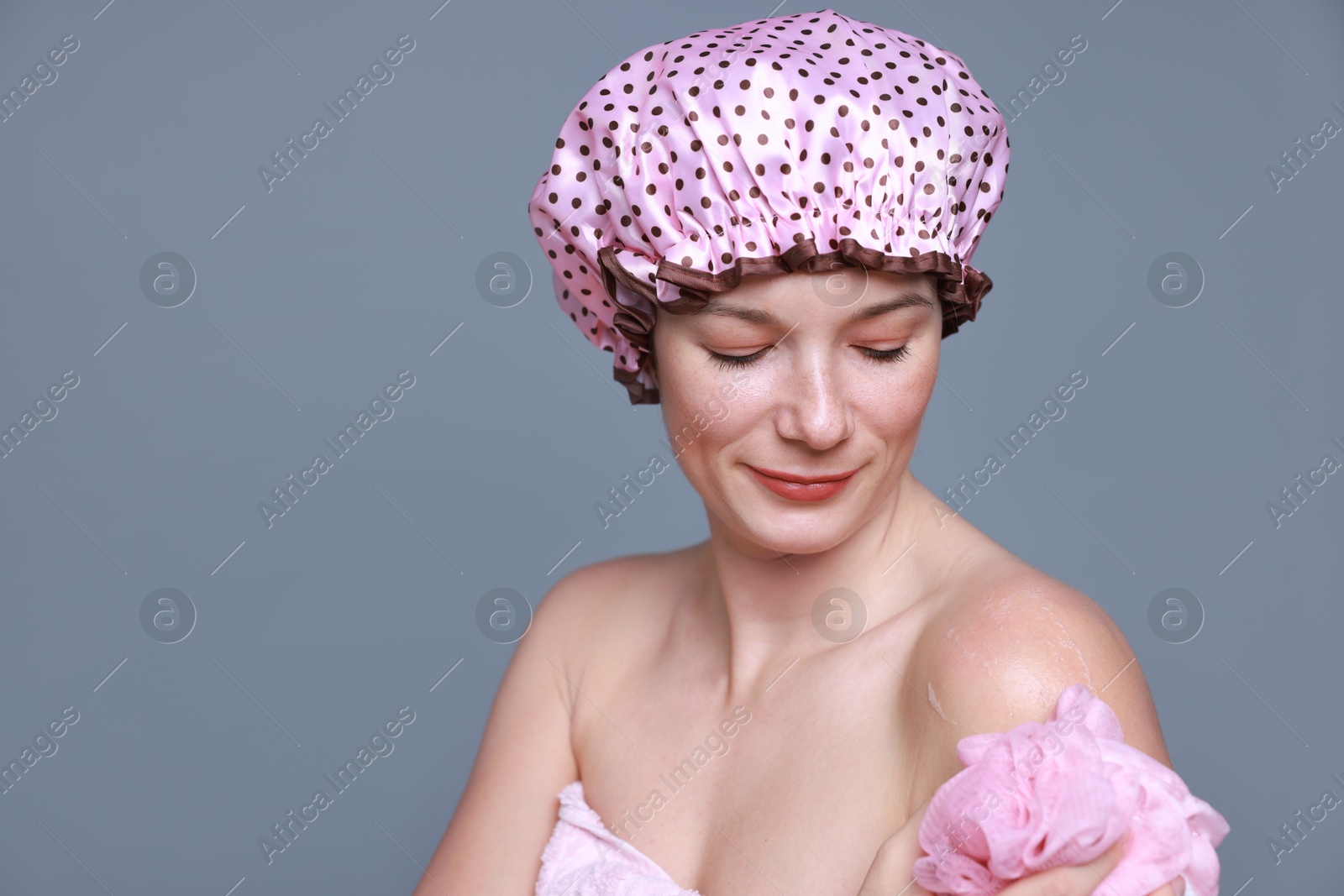 Photo of Woman with shower cap and mesh sponge on grey background, space for text