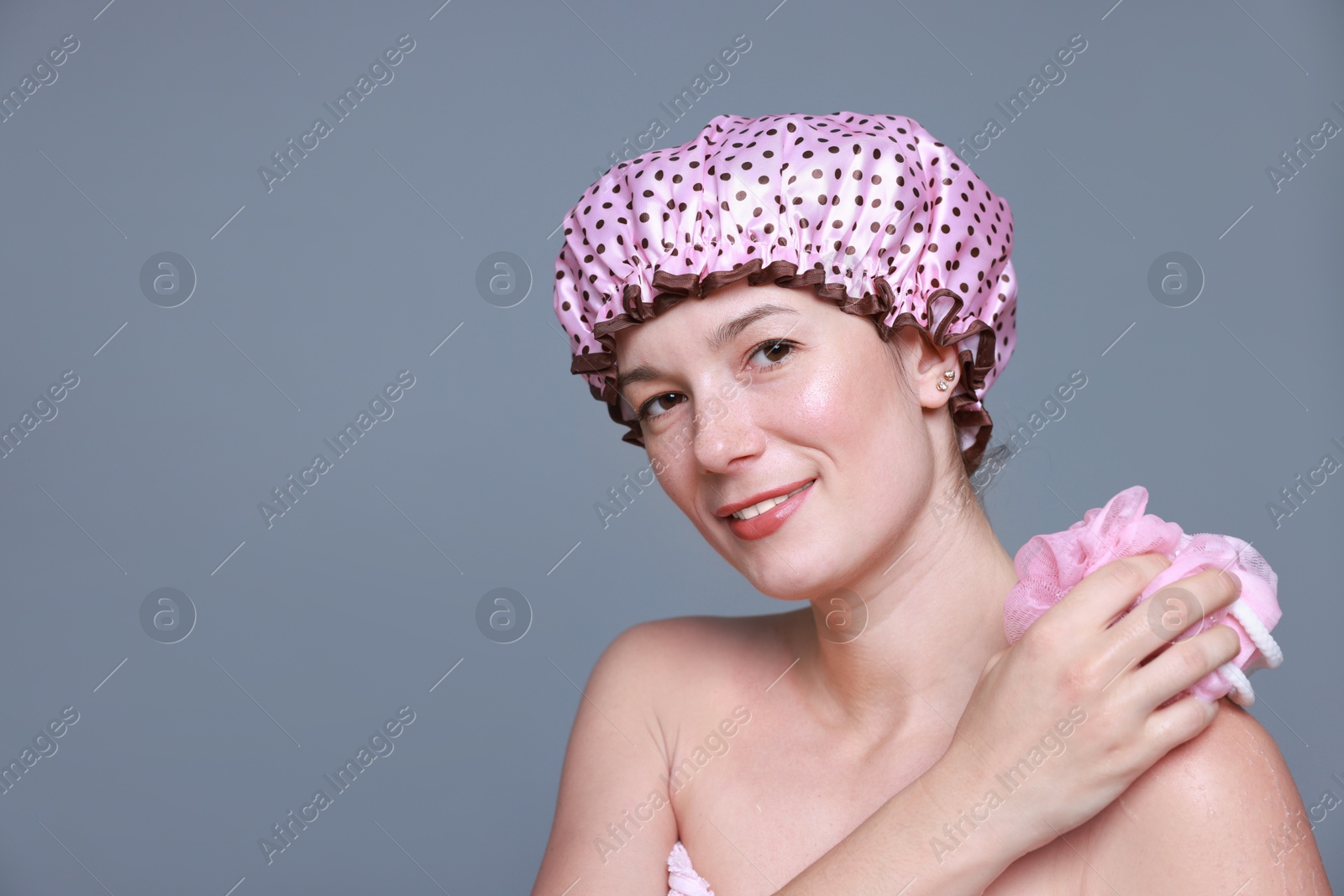 Photo of Woman with shower cap and mesh sponge on grey background, space for text