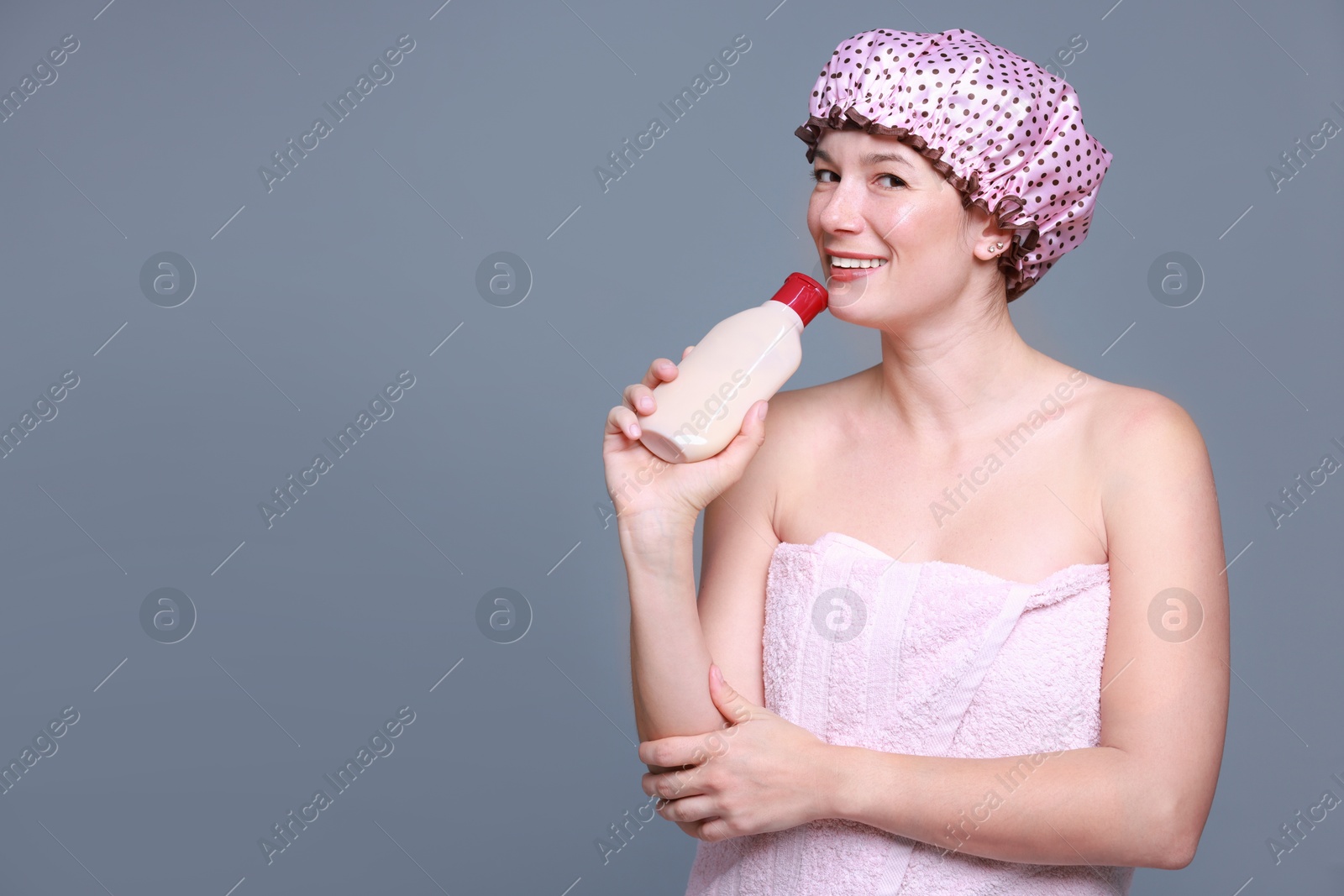 Photo of Woman with pink shower cap and shampoo on grey background, space for text