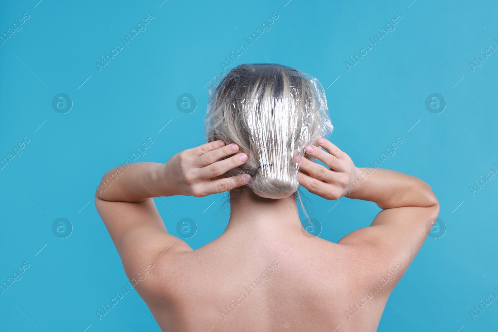 Photo of Woman wearing shower cap on light blue background, back view