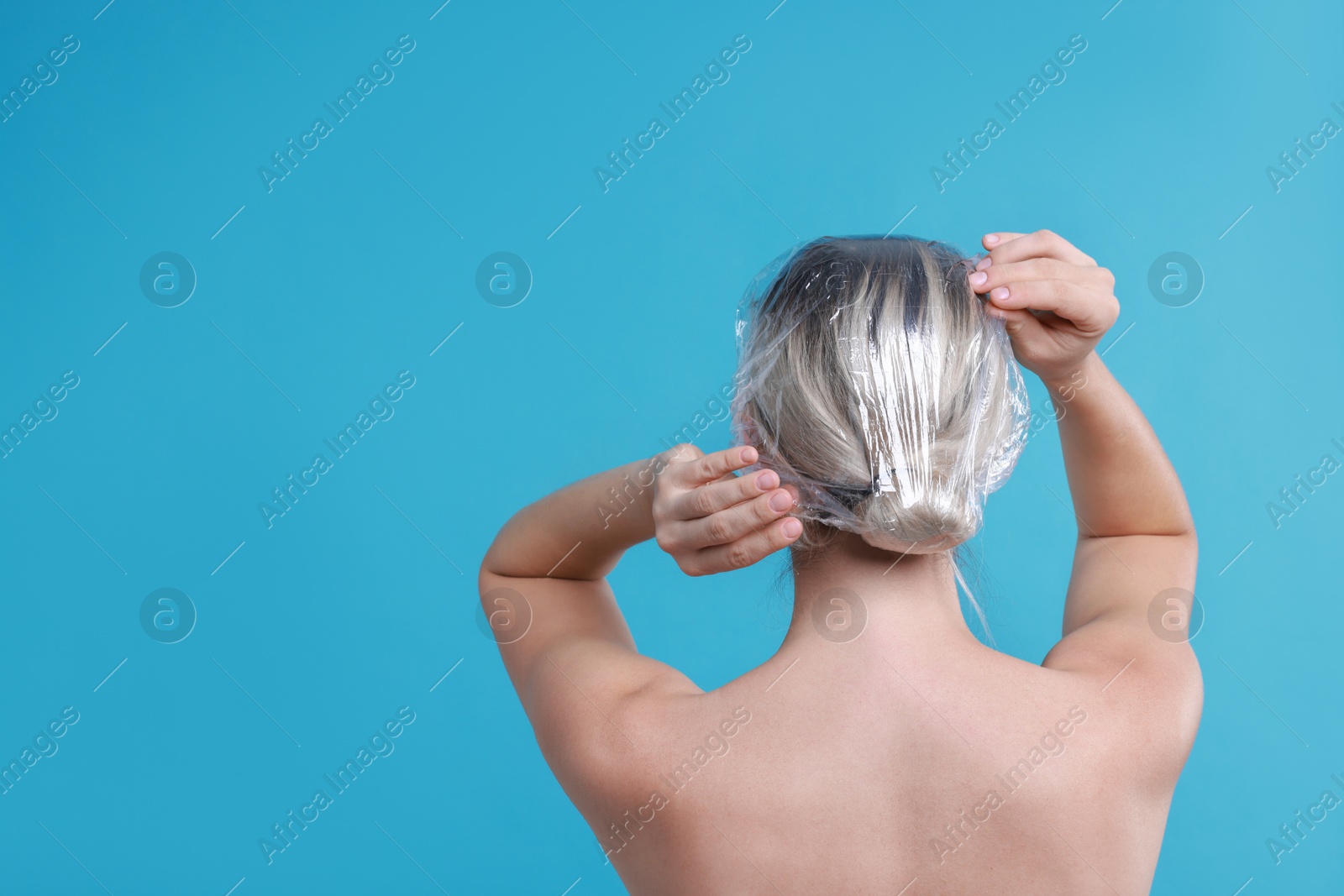 Photo of Woman wearing shower cap on light blue background, back view. Space for text