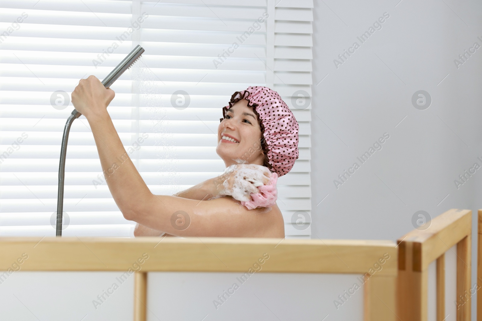 Photo of Woman with cap and mesh sponge taking shower in bathroom