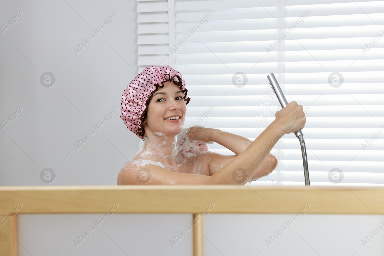 Photo of Woman with cap and mesh sponge taking shower in bathroom