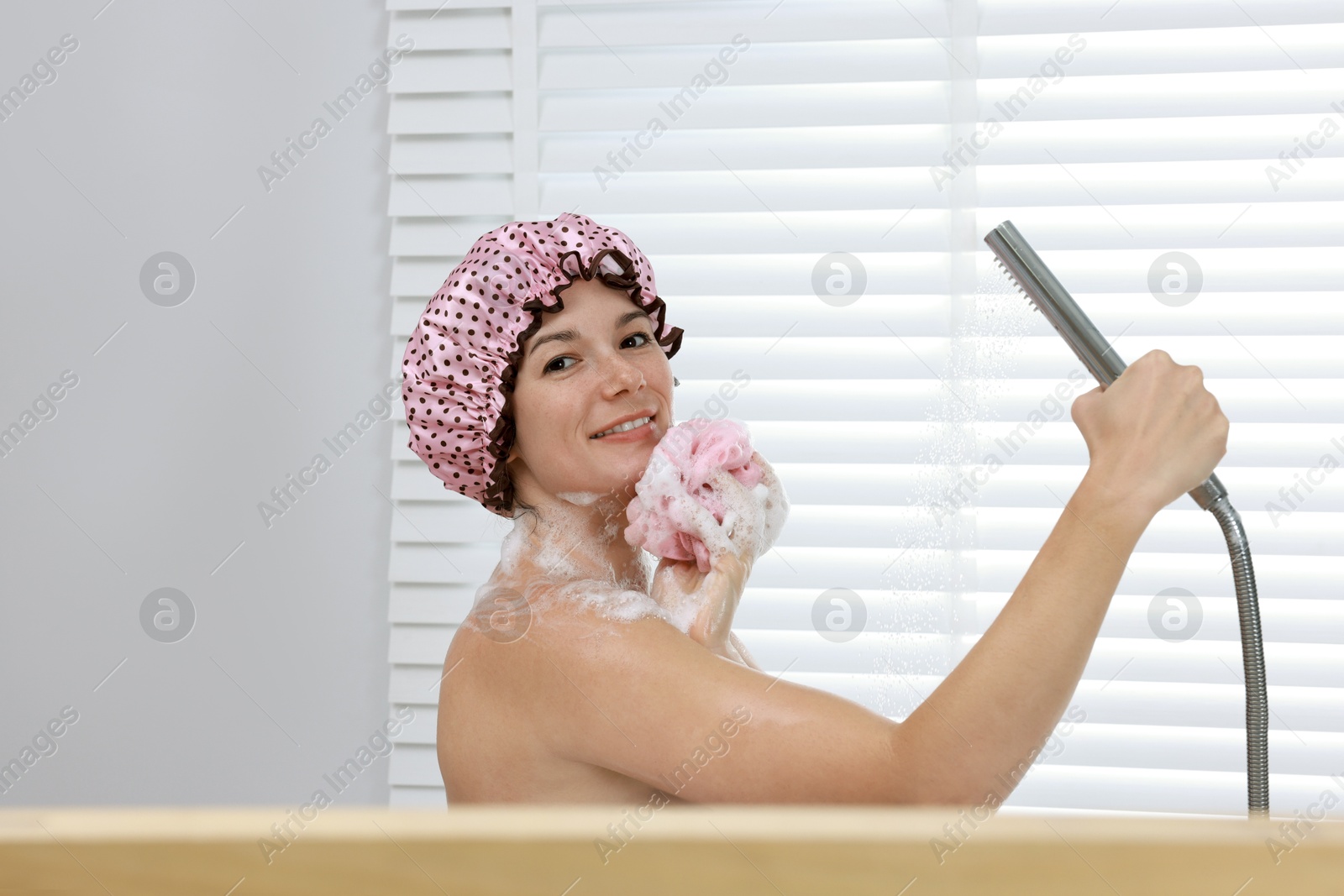 Photo of Woman with cap and mesh sponge taking shower in bathroom