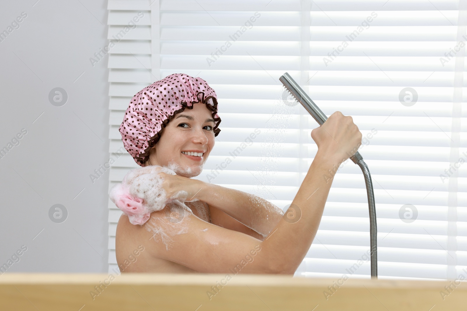 Photo of Woman with cap and mesh sponge taking shower in bathroom