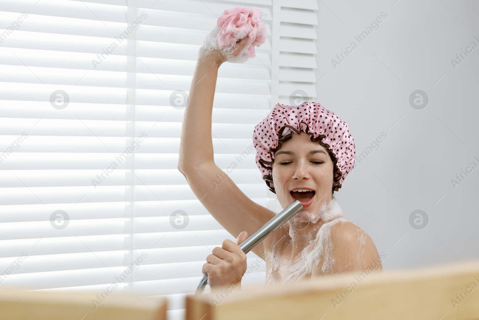 Photo of Woman with cap and mesh sponge singing while taking shower in bathroom, space for text