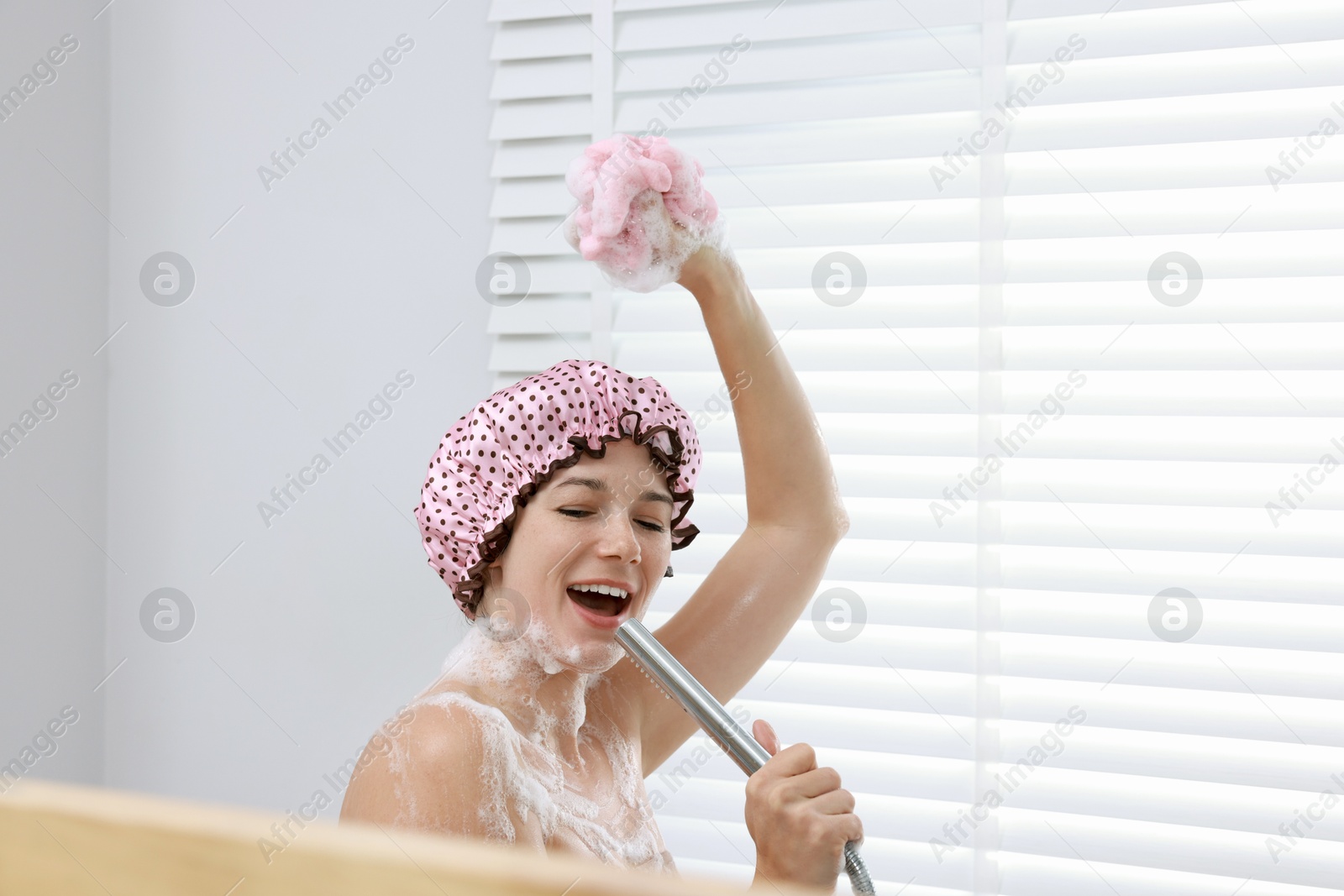 Photo of Woman with cap and mesh sponge singing while taking shower in bathroom, space for text