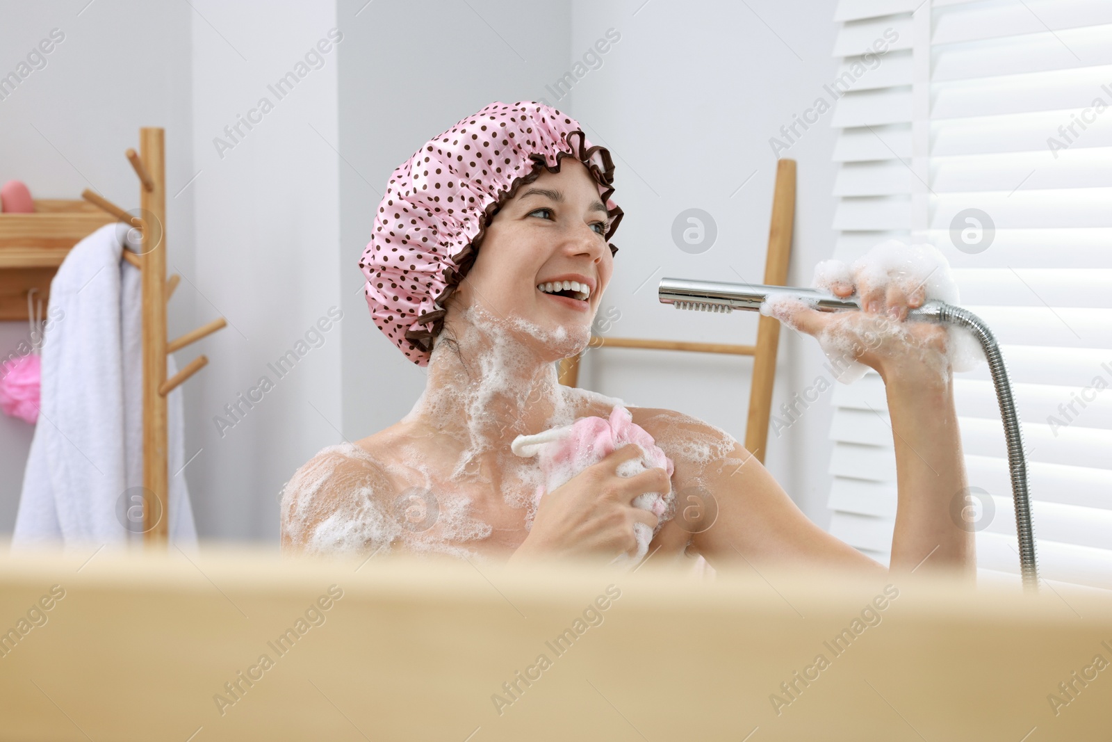 Photo of Woman with cap and mesh sponge singing while taking shower in bathroom