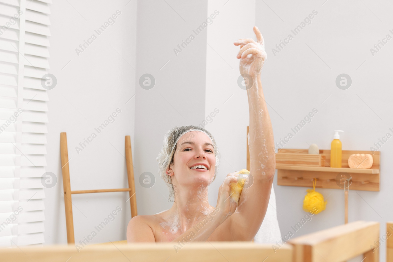 Photo of Woman with cap and mesh sponge taking shower in bathroom