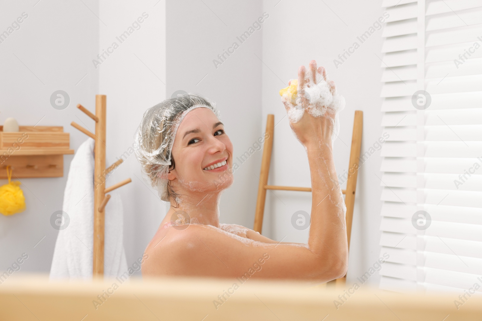 Photo of Woman with cap and mesh sponge taking shower in bathroom