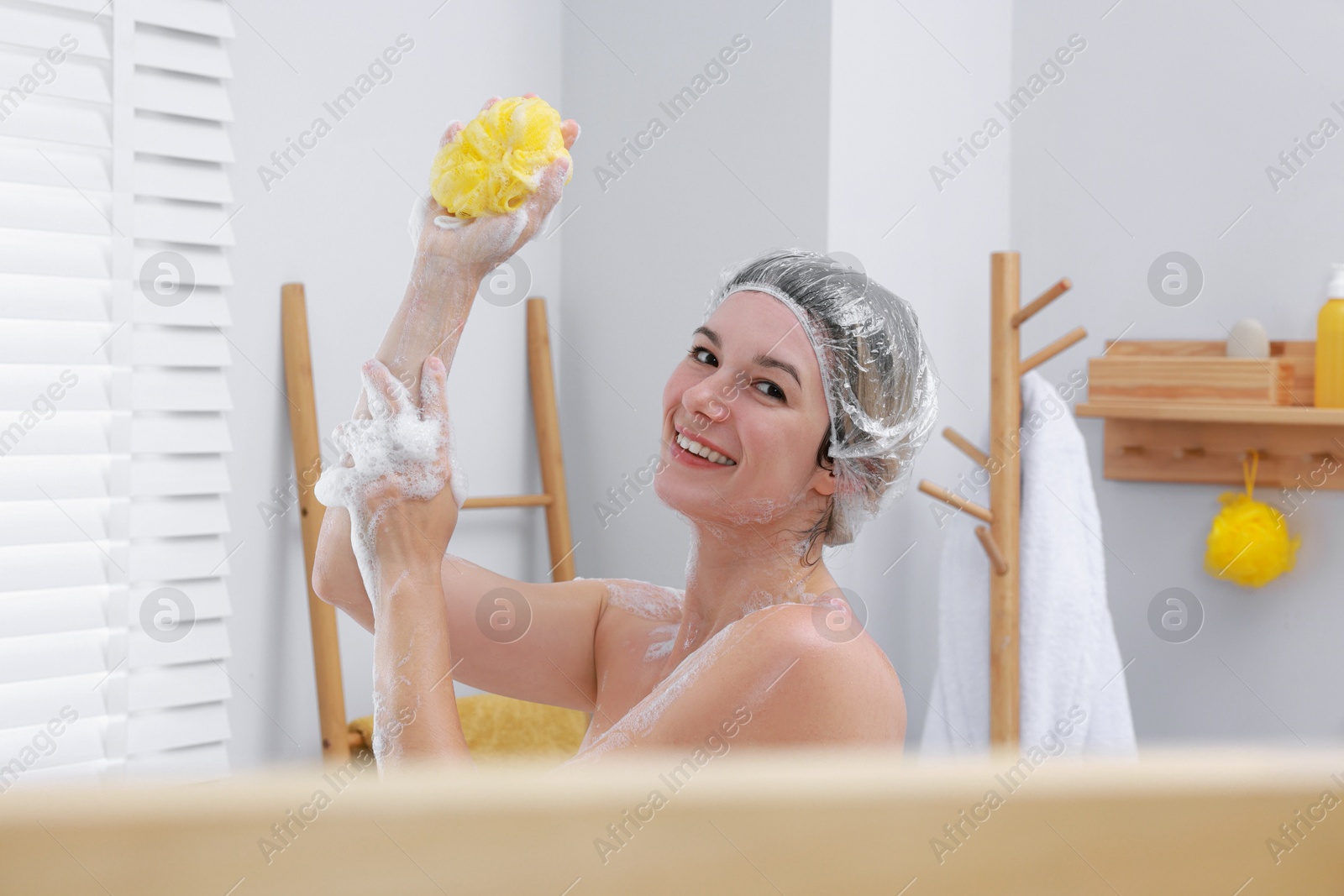 Photo of Woman with cap and mesh sponge taking shower in bathroom