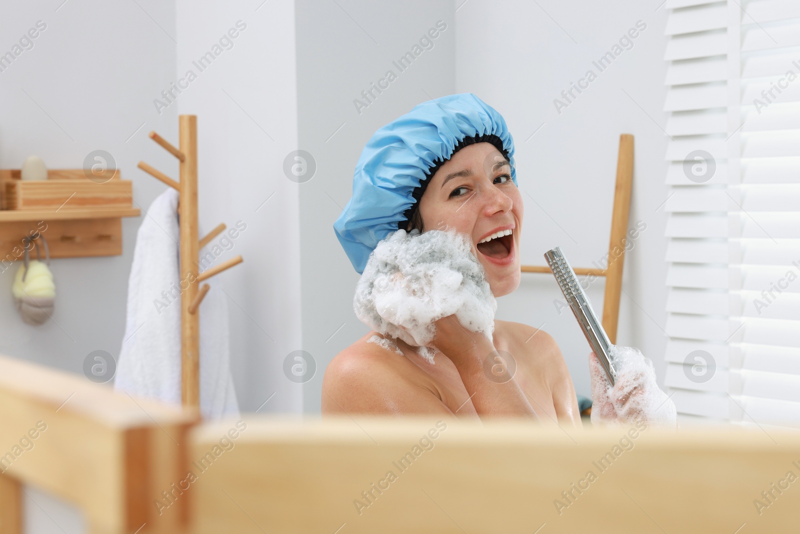 Photo of Woman with cap and mesh sponge singing while taking shower in bathroom