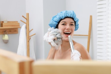 Photo of Woman with cap and mesh sponge singing while taking shower in bathroom