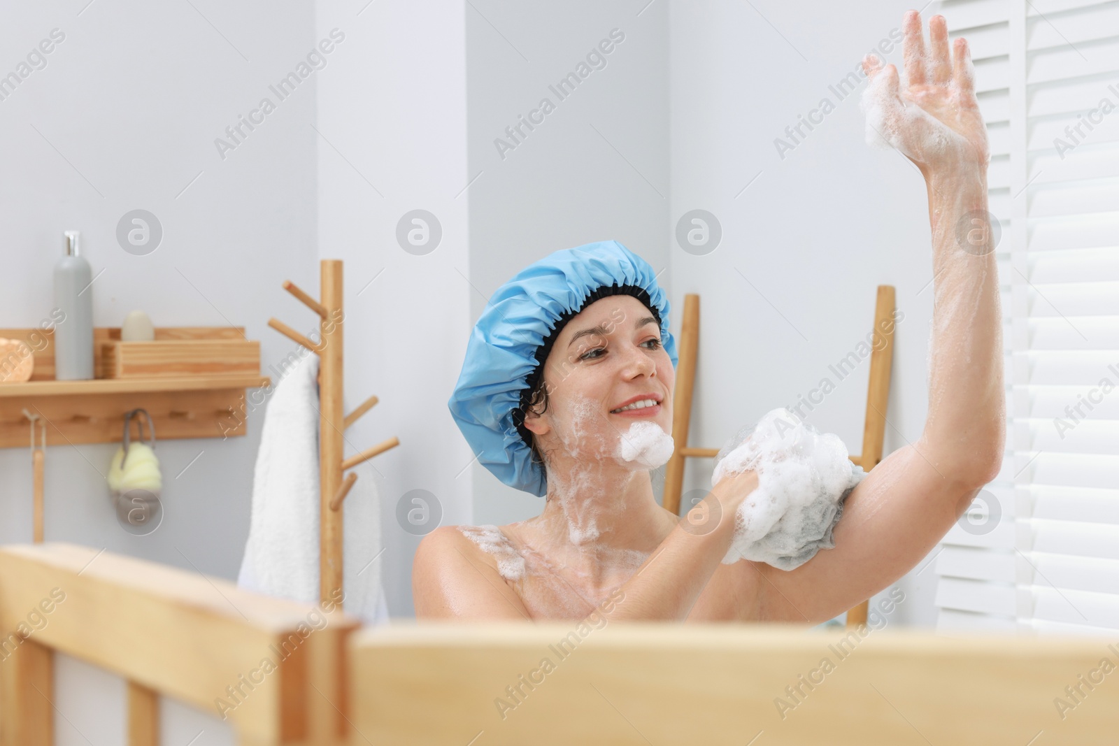 Photo of Woman with cap and mesh sponge taking shower in bathroom