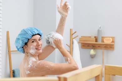 Photo of Woman with cap and mesh sponge taking shower in bathroom