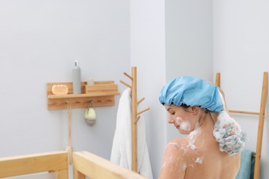 Photo of Woman with cap and mesh sponge taking shower in bathroom