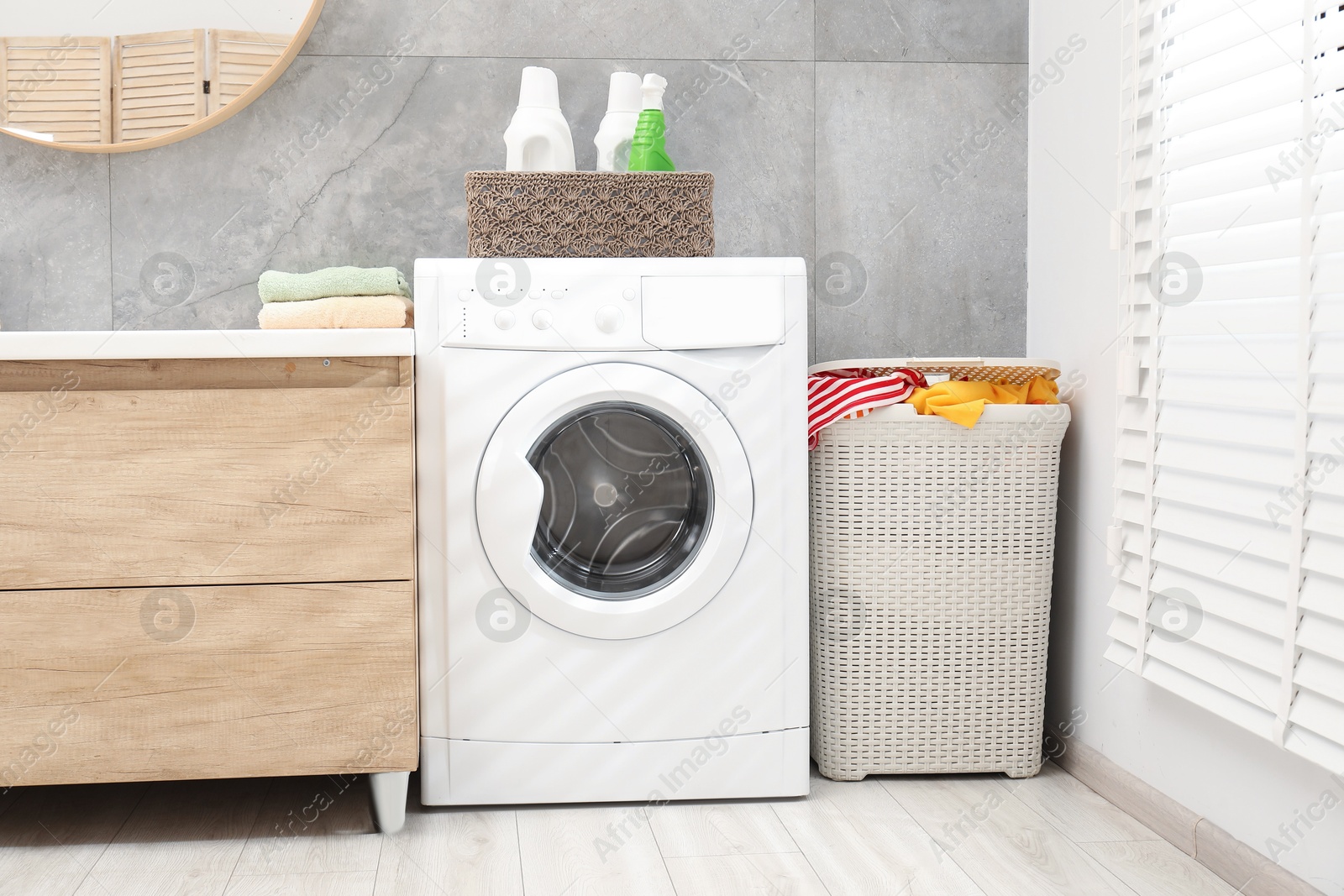 Photo of Wicker basket full of laundry, washing machine and detergents in bathroom