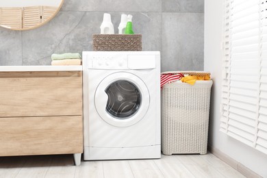 Photo of Wicker basket full of laundry, washing machine and detergents in bathroom