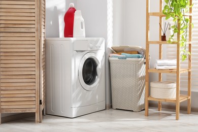 Photo of Wicker basket full of laundry, washing machine and detergents in bathroom