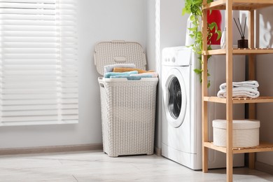 Photo of Wicker basket full of laundry and washing machine in bathroom