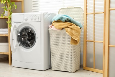 Photo of Wicker basket full of laundry and washing machine in bathroom