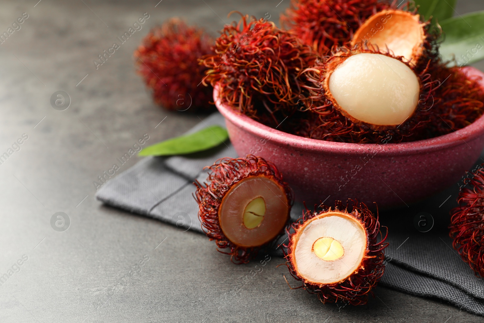 Photo of Delicious ripe rambutans and green leaves on grey table, closeup. Space for text